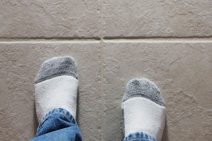 Feet with socks on hard ceramic tile floor under hard side light showing texture and detail with ivory grout lines.